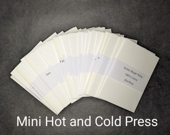 May include: A stack of bright white paper sheets, fanned out on a dark gray surface. The paper is labeled "Arches Bright White 100% Cotton Hot Press". The text "Mini Hot and Cold Press" is at the bottom.