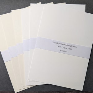 May include: A stack of watercolor paper sheets in varying shades of white and cream, bound with white bands. The top sheet displays text: "Saunders Waterford High White 100% Cotton, 140lb Hot Press."