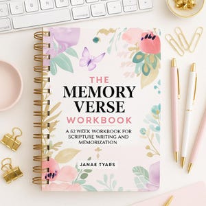 Puede incluir: Un cuaderno con espiral titulado "The Memory Verse Workbook" con ilustraciones florales y de mariposas. La portada presenta el texto "The Memory Verse Workbook" y "A 52 week workbook for scripture writing and memorization". También se ven bolígrafos y clips dorados.