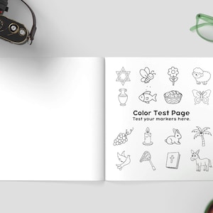 K&ouml;nnte beinhalten: Offenes Buch mit leerer linker Seite und rechter Seite mit einer "Color Test Page" mit Schwarz-Wei&szlig;-Illustrationen. Kamera, gr&uuml;ne Brille und eine Tasse Kaffee sind ebenfalls zu sehen.