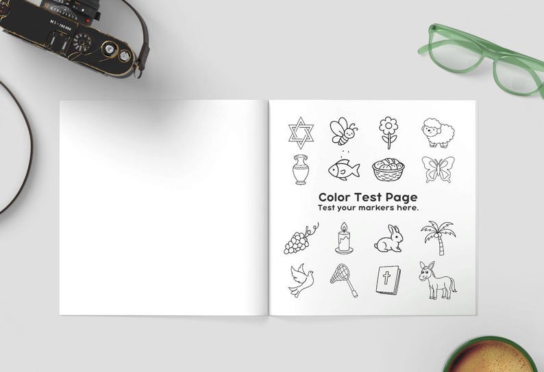 K&ouml;nnte beinhalten: Offenes Buch mit leerer linker Seite und rechter Seite mit einer "Color Test Page" mit Schwarz-Wei&szlig;-Illustrationen. Kamera, gr&uuml;ne Brille und eine Tasse Kaffee sind ebenfalls zu sehen.