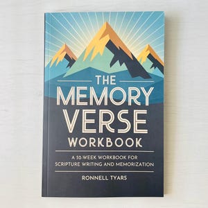 Può includere: Un quaderno con copertina rigida intitolato "The Memory Verse Workbook" con un'illustrazione di montagna nei toni del blu, dell'oro e del verde acqua. Il libro include il testo "A 52-Week Workbook for Scripture Writing and Memorization" e il nome dell'autore, Ronnell Tyars.