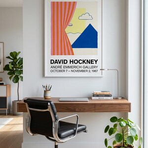 Op de afbeelding: Een moderne thuiskantoor met een zwevend houten bureau en een zwarte leren stoel. Een ingelijste David Hockney kunstprint hangt boven het bureau. Een potplant en een bureaulamp zijn ook zichtbaar.