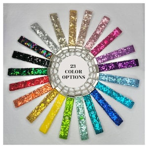 May include: A circle of 23 colorful keychains with sequins. The keychains are arranged in a circle around a silver key ring. The text "23 COLOR OPTIONS" is printed in the center of the circle.