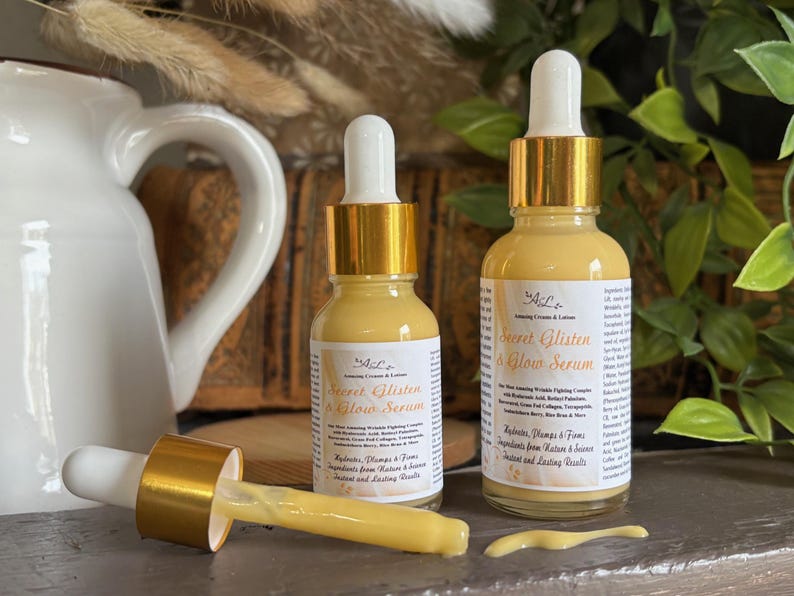 May include: Two amber glass bottles with gold lids and droppers filled with a yellow serum. The bottles are labeled "Secret Glisten & Glow Serum" and contain ingredients from nature for instant and lasting results.