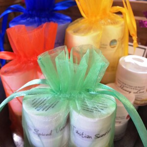 May include: A collection of small, cylindrical containers, likely beauty products, are presented in colorful tulle bags. The bags are tied with matching ribbons in blue, orange, yellow, and green. The labels on the containers read "Spiced Vanilla" and "Tahitian Sunrise."