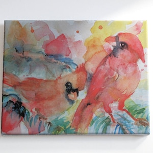 Original watercolor painting of two red cardinals sitting on loosely painted blue spruce branches has been printed onto matte canvas that has been stretched on a wood frame.  Colorful painting done mainly in reds, yellow, blues and green.