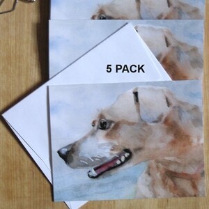 A 5 pack set of hound dog cards are displayed on a wood table with postage stamps and butterfly paper clips. Printed from my watercolor painting of this cute pup's head shown in profile with clouds in the background.  White envelopes included.