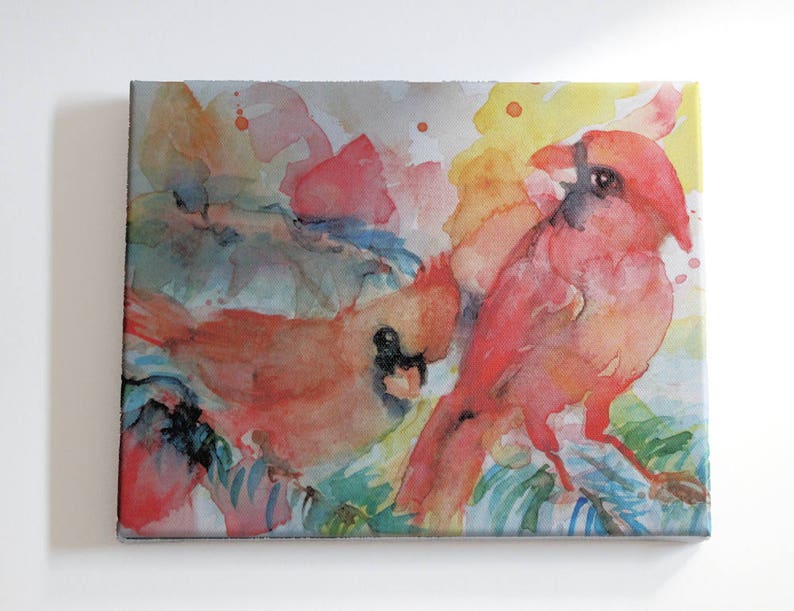 Original watercolor painting of two red cardinals sitting on loosely painted blue spruce branches has been printed onto matte canvas that has been stretched on a wood frame.  Colorful painting done mainly in reds, yellow, blues and green.