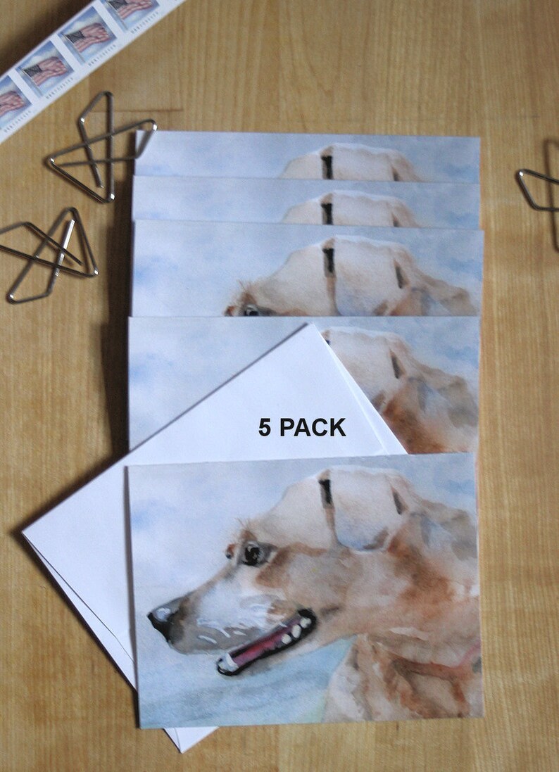 A 5 pack set of hound dog cards are displayed on a wood table with postage stamps and butterfly paper clips. Printed from my watercolor painting of this cute pup's head shown in profile with clouds in the background.  White envelopes included.