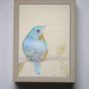 K&ouml;nnte beinhalten: Ein gerahmtes Aquarellbild eines blauen Vogels, der auf einem Ast sitzt. Der Vogel schaut nach rechts und hat eine gelbe Brust. Der Hintergrund ist hellgelb.