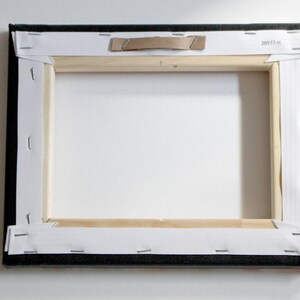 View from the back of the canvas print.  Canvas on the back is white in color, folded neatly at the corners and stapled to a wooden frame.  A metal hanger is covered by cardboard for protection in shipping.