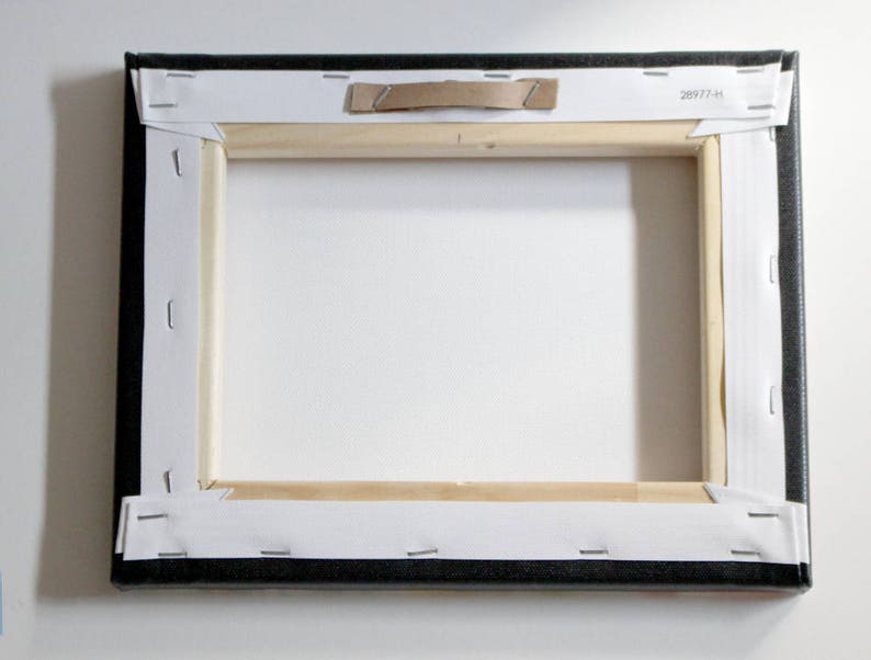 View from the back of the canvas print.  Canvas on the back is white in color, folded neatly at the corners and stapled to a wooden frame.  A metal hanger is covered by cardboard for protection in shipping.