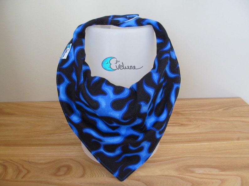 May include: A blue and black bandana with a flame pattern. The bandana is folded in a triangle shape. The bandana is made of fabric and has a tag on the side.
