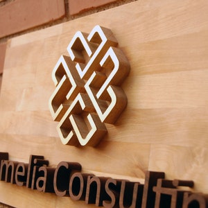 May include: A wooden sign with a gold-colored knot design and the text "Amelia Consulting" in brown raised letters.