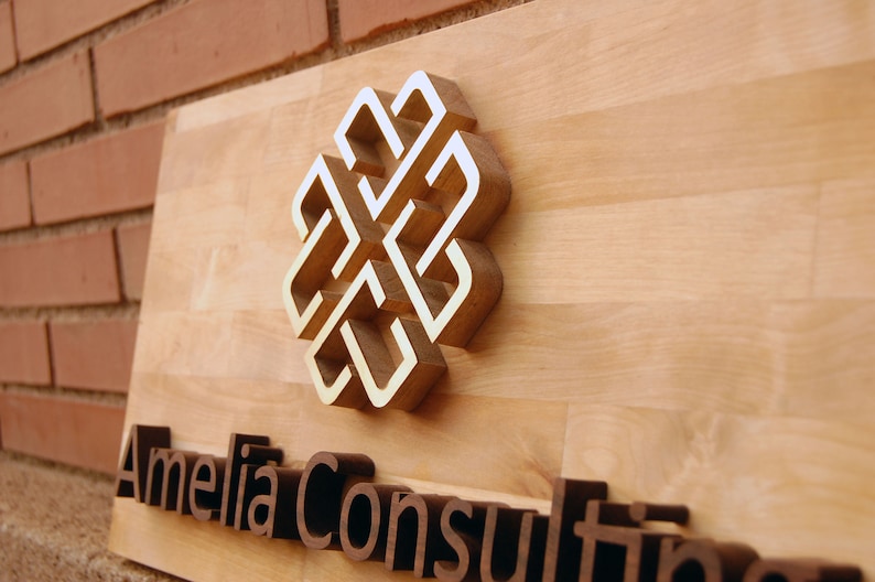 May include: A wooden sign with a gold-colored knot design and the text "Amelia Consulting" in brown raised letters.