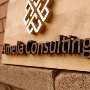May include: A wooden sign with the text "Amelia Consulting" in brown raised letters. A gold-colored geometric design is above the text.