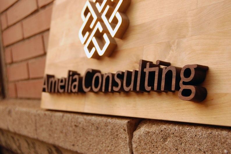 May include: A wooden sign with the text "Amelia Consulting" in brown raised letters. A gold-colored geometric design is above the text.