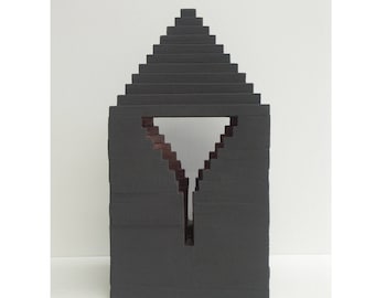 May include: A black geometric sculpture made of stacked rectangular blocks. The sculpture has a triangular opening in the center.