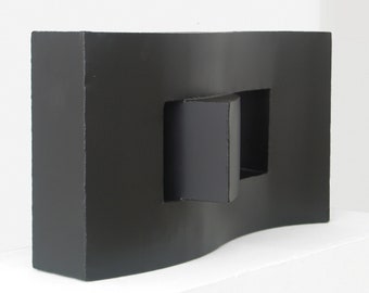 May include: A black abstract sculpture with a rectangular opening in the center. The sculpture has a wavy, organic shape.