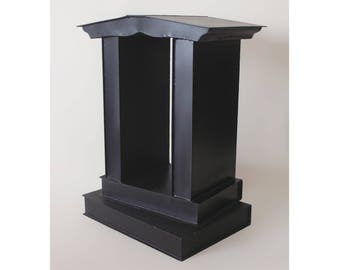 May include: A black metal stand with a rectangular base and two pillars. The stand has a flat top and a decorative design on the top edge.