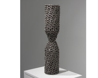 May include: A tall, silver sculpture made of linked metal chains. The sculpture is shaped like a vase with a narrow waist.