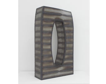 May include: A tall, rectangular sculpture made of metal with a large, oval opening in the center. The sculpture is made of many thin, horizontal strips of metal that are welded together. The metal has a dark, weathered finish.