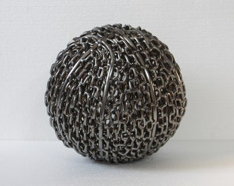 May include: A large, spherical sculpture made entirely of interlocking metal chains. The sculpture is silver in color and has a smooth, polished finish.