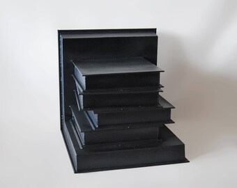 May include: A black, rectangular, tiered display stand with five levels. The stand is made of a smooth, solid material and has a modern, minimalist design.