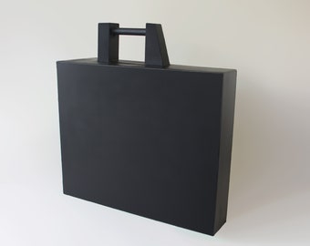May include: A black rectangular box with a handle on top. The box is made of a sturdy material and has a smooth, matte finish.