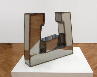 May include: Abstract sculpture made of metal with a white, brown, and silver finish. The sculpture is composed of geometric shapes and is displayed on a white pedestal.