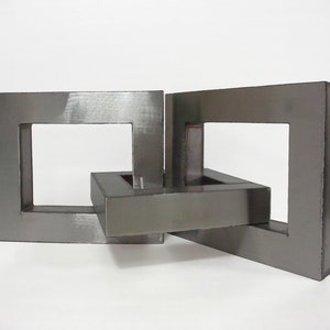 Könnte beinhalten: Eine silberne Metallskulptur aus zwei ineinandergreifenden Quadraten. Die Skulptur ist aus poliertem Metall gefertigt und hat ein modernes, minimalistisches Design.