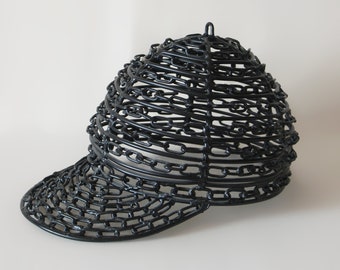 May include: A black baseball cap made entirely of linked chains. The cap has a curved brim and a rounded crown.