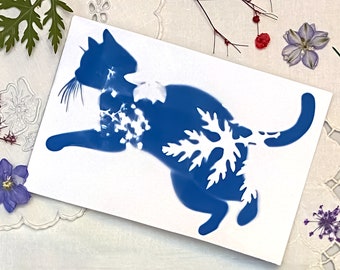 May include: A blue silhouette of a cat with a white snowflake design on its back. The image is printed on white paper.