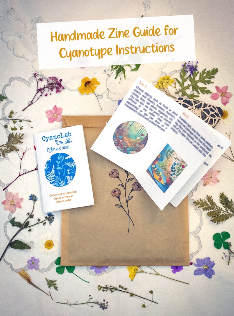 May include: A brown paper envelope with a small blue booklet titled "CyanoLab Instructions" and a folded white booklet with instructions for creating cyanotype prints. The envelope is surrounded by dried flowers and leaves on a white lace tablecloth.