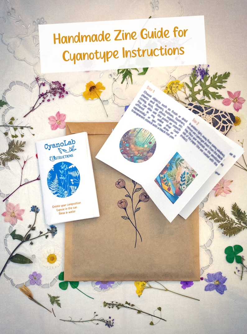 May include: A brown paper envelope with a small blue booklet titled "CyanoLab Instructions" and a folded white booklet with instructions for creating cyanotype prints. The envelope is surrounded by dried flowers and leaves on a white lace tablecloth.