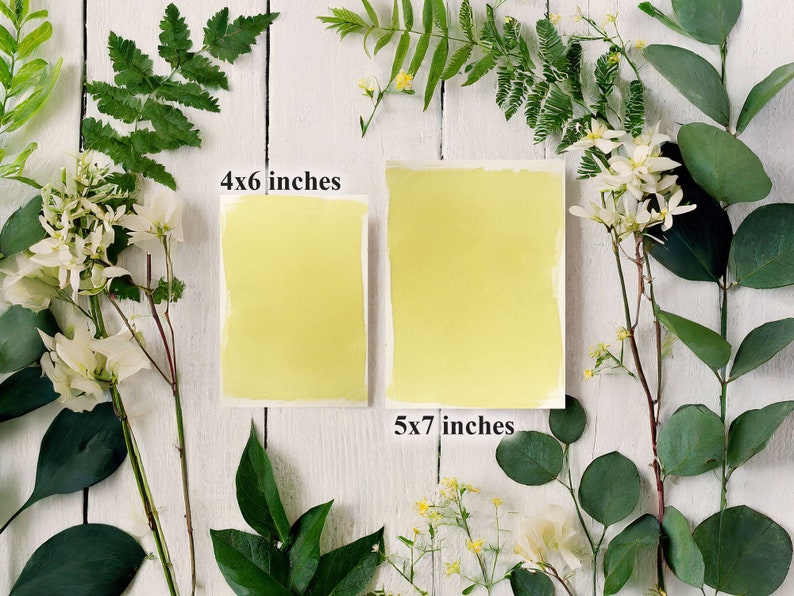 May include: Two yellow cardstock paper sheets on a white wooden background. The sheet on the left is 4x6 inches and the sheet on the right is 5x7 inches. The sheets are surrounded by green leaves and white flowers.
