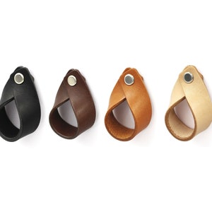 Könnte beinhalten: Vier Leder-Schubladengriffe in Schwarz, Braun, Beige und Creme. Jeder Griff hat einen silbernen Metallknopf.