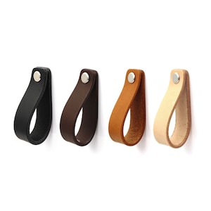 Könnte beinhalten: Vier Leder-Schubladengriffe in verschiedenen Farben: Schwarz, Braun, Beige und Natur. Jeder Griff hat einen silbernen Metallnieten.