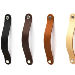 Könnte beinhalten: Vier Leder-Schrankgriffe in Schwarz, Braun, Beige und Hellbeige mit silbernen Metallakzenten.
