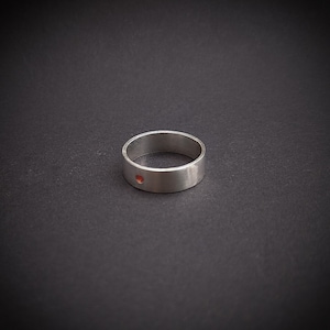 May include: A silver ring with a small red dot in the centre.
