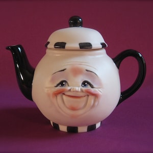May include: A white teapot with a black and white striped design. The teapot has a face with a smiling expression and black eyes.