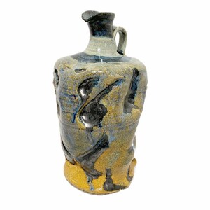 Puede incluir: Jarra de cerámica hecha a mano con asa y boquilla. La jarra presenta una superficie texturizada con una mezcla de esmaltes azules, negros y amarillo-marrón. La base es de color amarillo-dorado brillante.