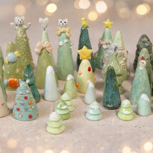 Pode incluir: Uma coleção de árvores de Natal de cerâmica em vários tamanhos e designs. As árvores são principalmente verdes, com elementos decorativos como estrelas, corações e laços. Algumas árvores têm uma aparência texturizada, outras são lisas.