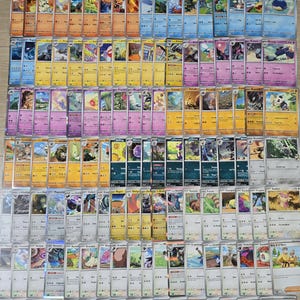 May include: A collection of colorful trading cards, featuring various characters and designs. The cards are arranged in neat rows, showcasing a variety of artwork and card types. The cards are in protective sleeves.