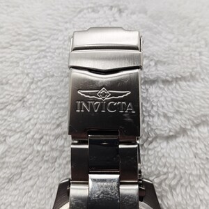Puede incluir: Primer plano de un cierre de reloj Invicta plateado. El cierre es rectangular con el nombre de la marca y el logotipo grabados en la parte delantera. La correa del reloj tambi&eacute;n es plateada y parece ser de metal.