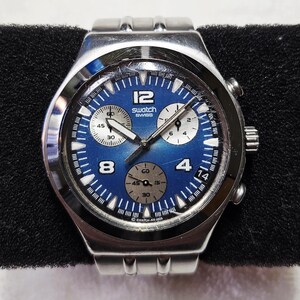 May include: A Swatch Swiss chronograph watch with a blue dial and silver-tone stainless steel band. The watch face features white numerals and sub-dials. The watch is displayed on a black surface.