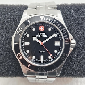 May include: A stainless steel Swiss Military watch with a black dial and a rotating bezel. The watch face features white hands and markers, a date window, and the text "SWISS MILITARY" and "200M". The watch is displayed on a black surface.
