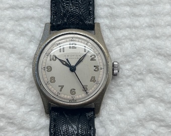 Puede incluir: Un reloj de pulsera plateado con una esfera blanca y agujas negras. El reloj tiene una correa de cuero negra y dice "Croton Resistal" en la esfera.