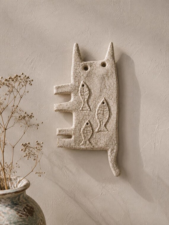 A one-of-a-kind handmade clay cat wall sculpture blending folk art and mythology — the kind of weird, soulful piece that stops guests in their tracks.